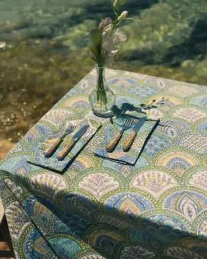 Mantel India de algodón con estampado ornamental en tonos azul, verde y beige sobre mesa decorada frente al mar.