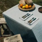 Mantel Rayas Azul de algodón con diseño de rayas blancas y azules sobre una mesa exterior junto al mar.