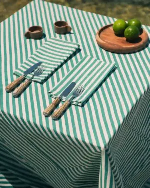 Mantel de rayas verdes y blancas de Cassai con servilletas a juego, cubiertos de fibras naturales y limas sobre mesa de inspiración mediterránea.