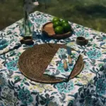 Mantel Cupido Azul de algodón con estampado floral en tonos azules y verdes sobre una mesa decorada con servilletas, limas y fibras naturales.