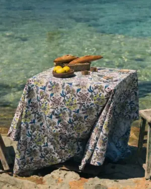Mantel Cupido Gris de algodón con estampado floral en tonos gris, azul y verde sobre una mesa exterior junto al mar.