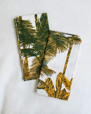 Servilletas de tela de algodón con estampado de palmeras en tonos verde y mostaza sobre fondo blanco, diseño de inspiración mediterránea.