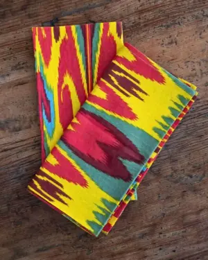Juego de servilletas de algodón Ikat Arcoíris con estampado étnico multicolor sobre mesa de madera.