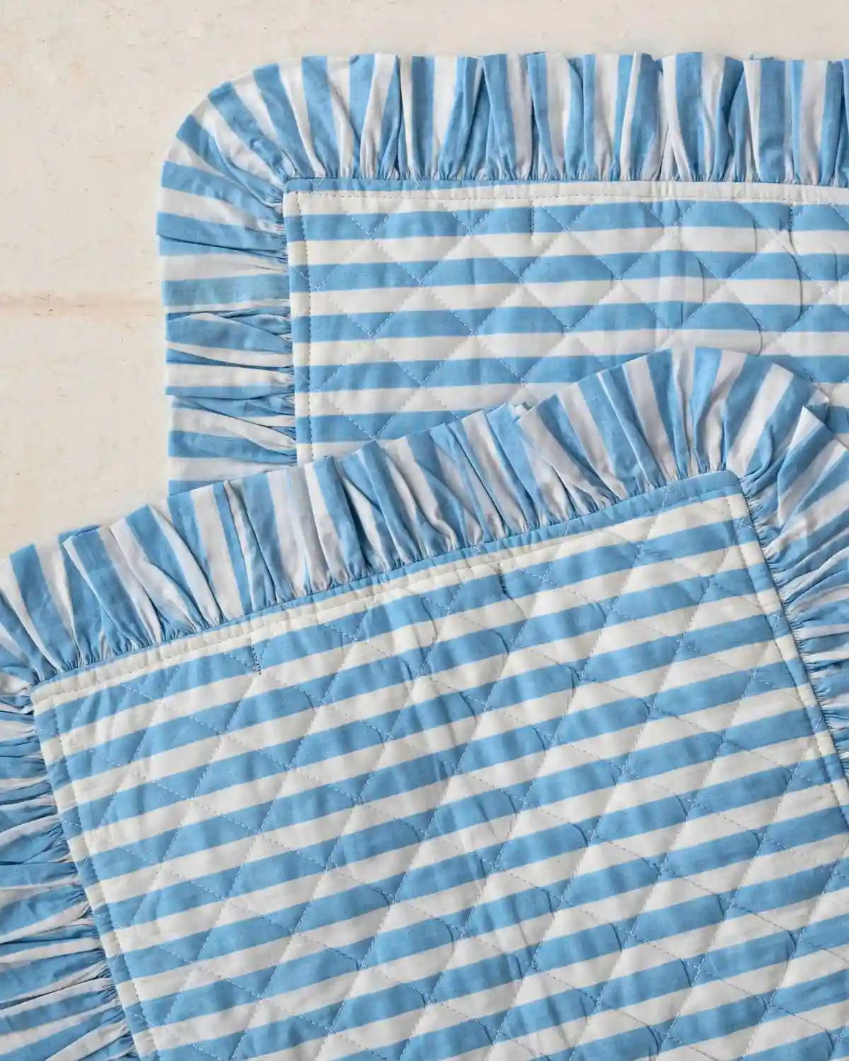 Mantel individual de algodón con rayas azules y volante plisado para una mesa luminosa de inspiración mediterránea.