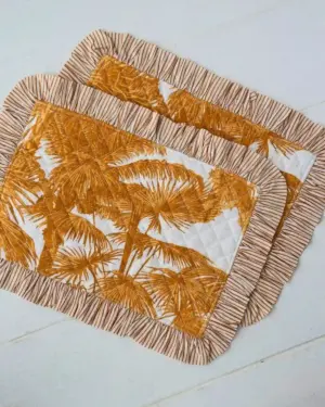 Set de individuales acolchados Palmera Mostaza con volante y estampado tropical en tonos mostaza y blanco de Cassai.