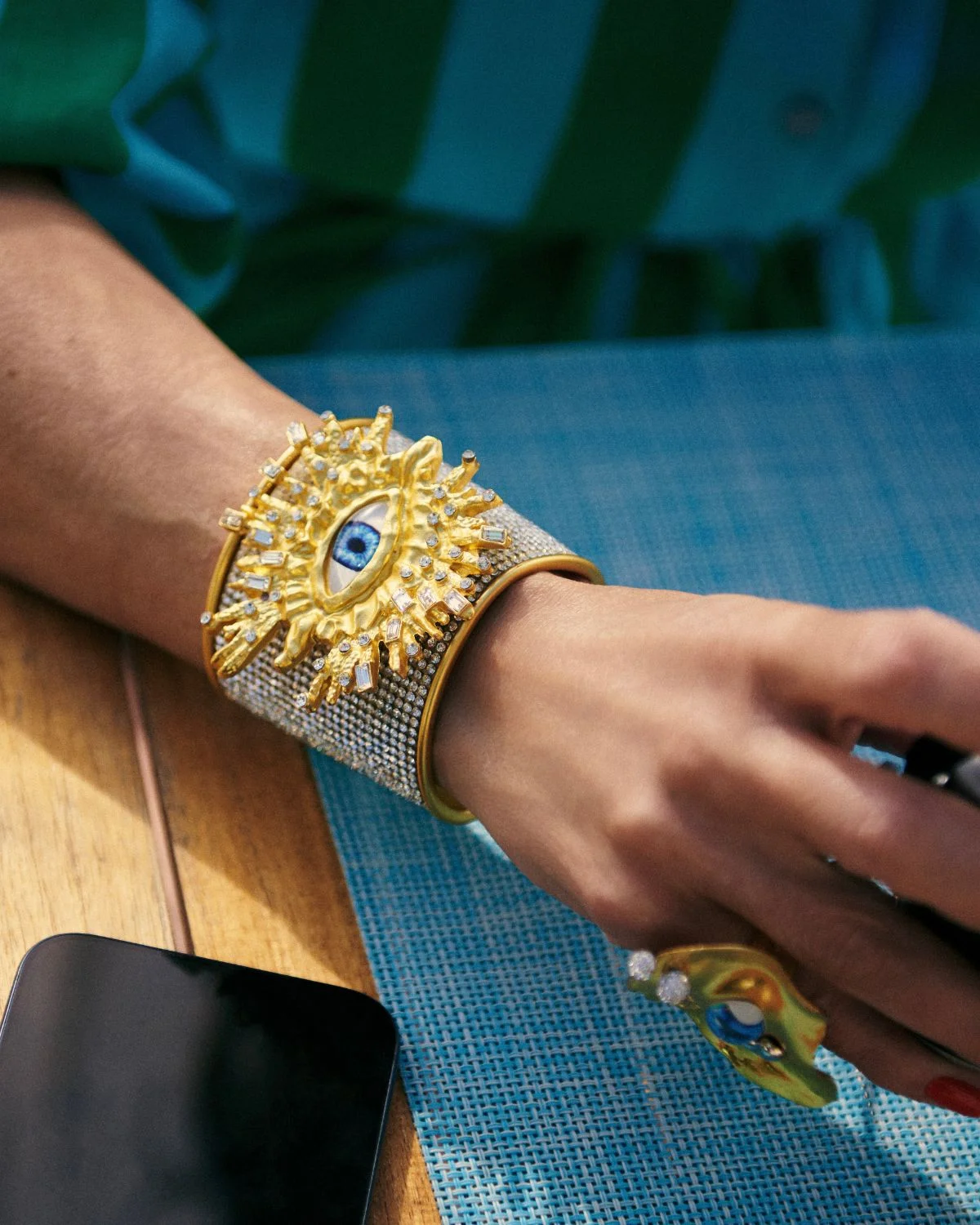 El Brazalete Dorado Ojos de Zeus destaca por su estructura tipo cuff con malla de microcristales y un diseño radial central que aporta una estética mística y sofisticada.