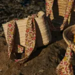 Cesta de palmito pequeña con asas de estampado floral sobre rocas junto al mar estilo mediterráneo