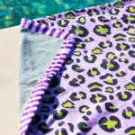 Toalla de playa animal print lila con estampado de leopardo en negro y verde, reverso gris y ribete a rayas. Diseño original en algodón. Cassai Home Mallorca.