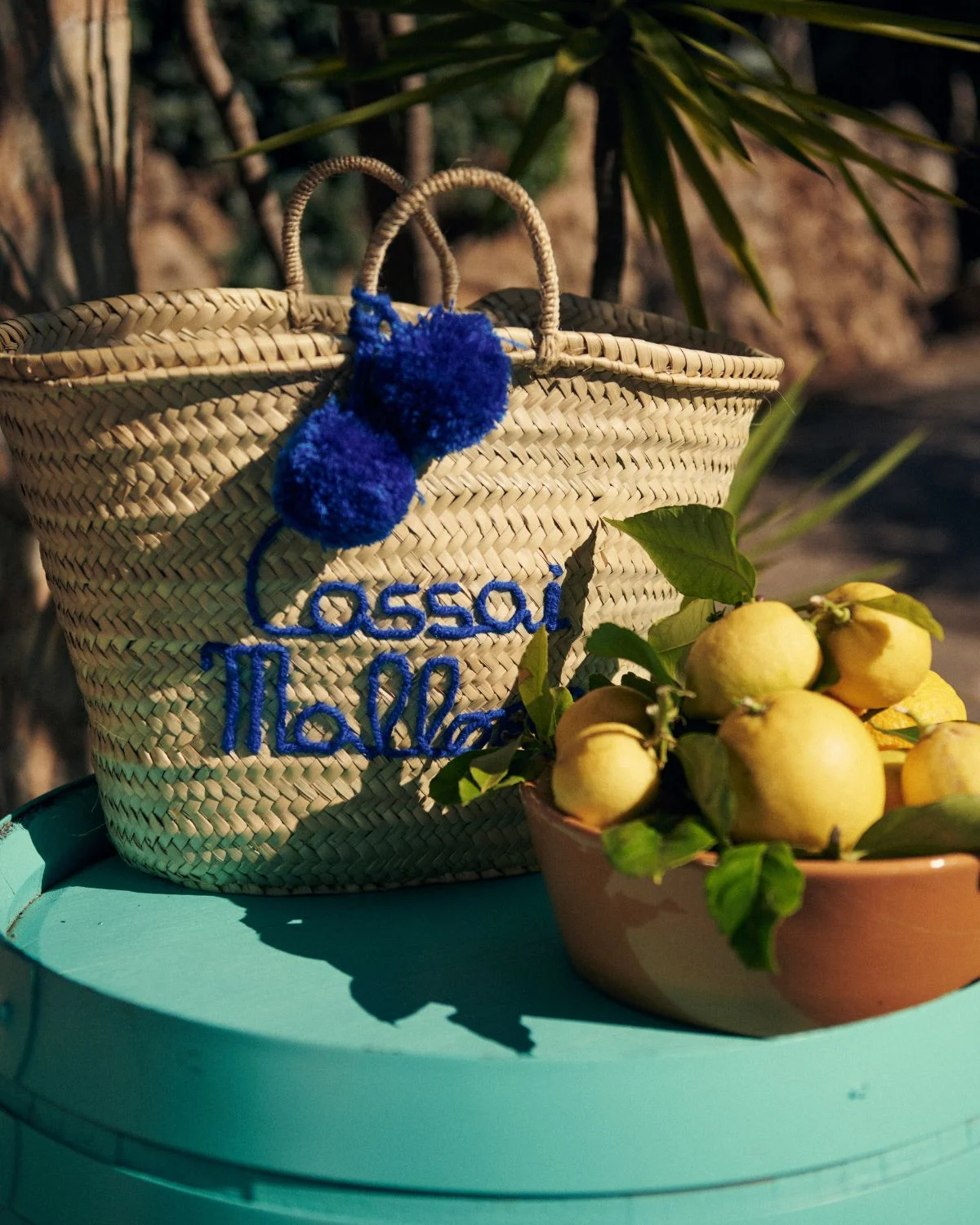Capazo de playa de palmito con bordado azul y borla decorativa, inspirado en la estética mediterránea.