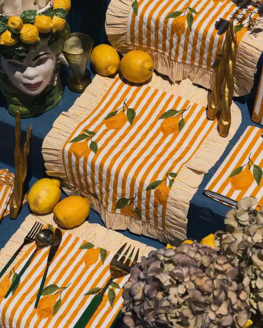 Mantel individual acolchado con rayas amarillas, estampado de limones y volante decorativo para vestir la mesa con inspiración mediterránea.