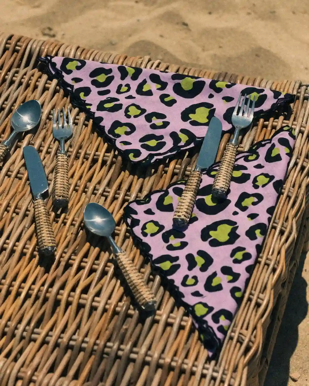 Servilletas de tela Animal Print Lila con borde festoneado, acompañadas de cubiertos de ratán.