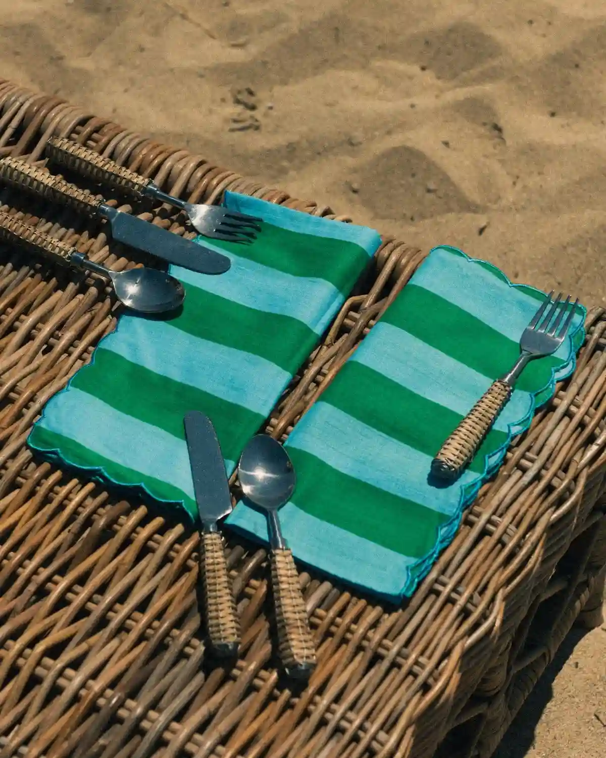 Servilletas de tela a rayas menta y verde con borde festoneado, acompañadas de cubiertos de ratán.