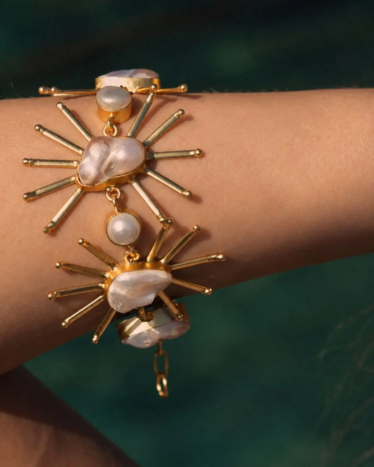 Brazalete Llum dorado con diseño de sol y perlas de formas orgánicas.