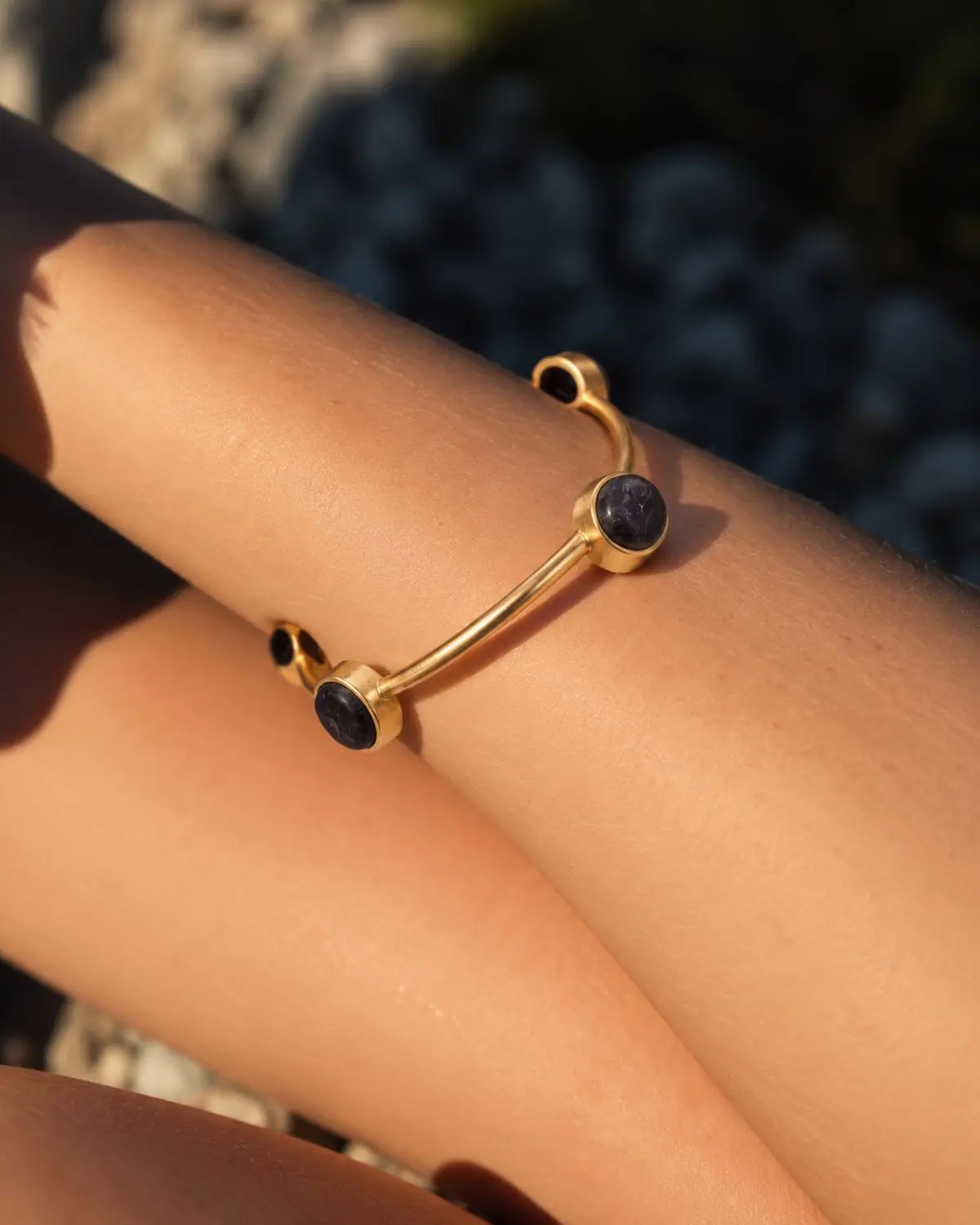 Brazalete Minimalista dorado de diseño rígido con piedras negras circulares.