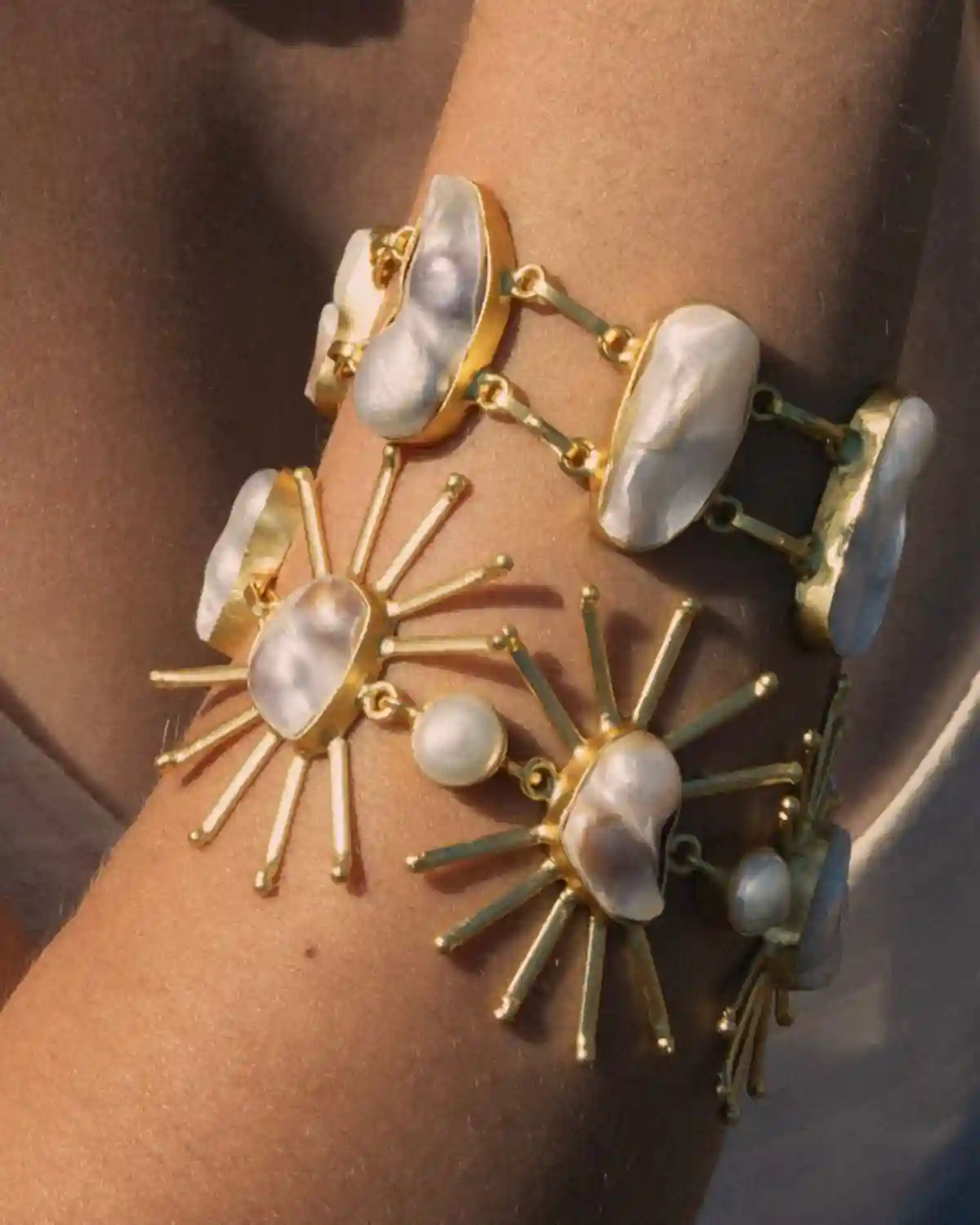 Brazalete dorado Calma y collar de perla barroca en un look de inspiración mediterránea.