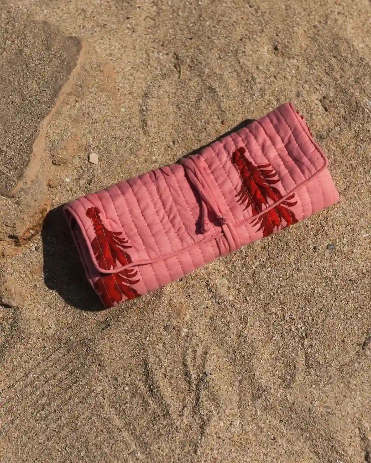 Bolsa de maquillaje acolchada con langostas rojo burdeos sobre fondo rosa, enrollada y cerrada con cordón a juego.