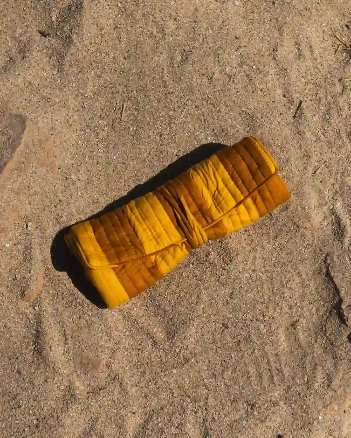 Bolsa de maquillaje acolchada en tonos mostaza y ocre, enrollada y cerrada con cordón a juego.