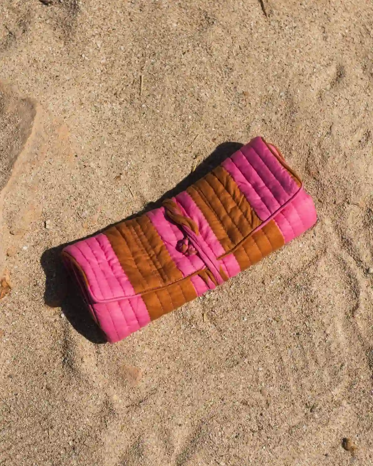 Bolsa de maquillaje acolchada de rayas rosa y mostaza con cierre enrollable y cordón a juego.