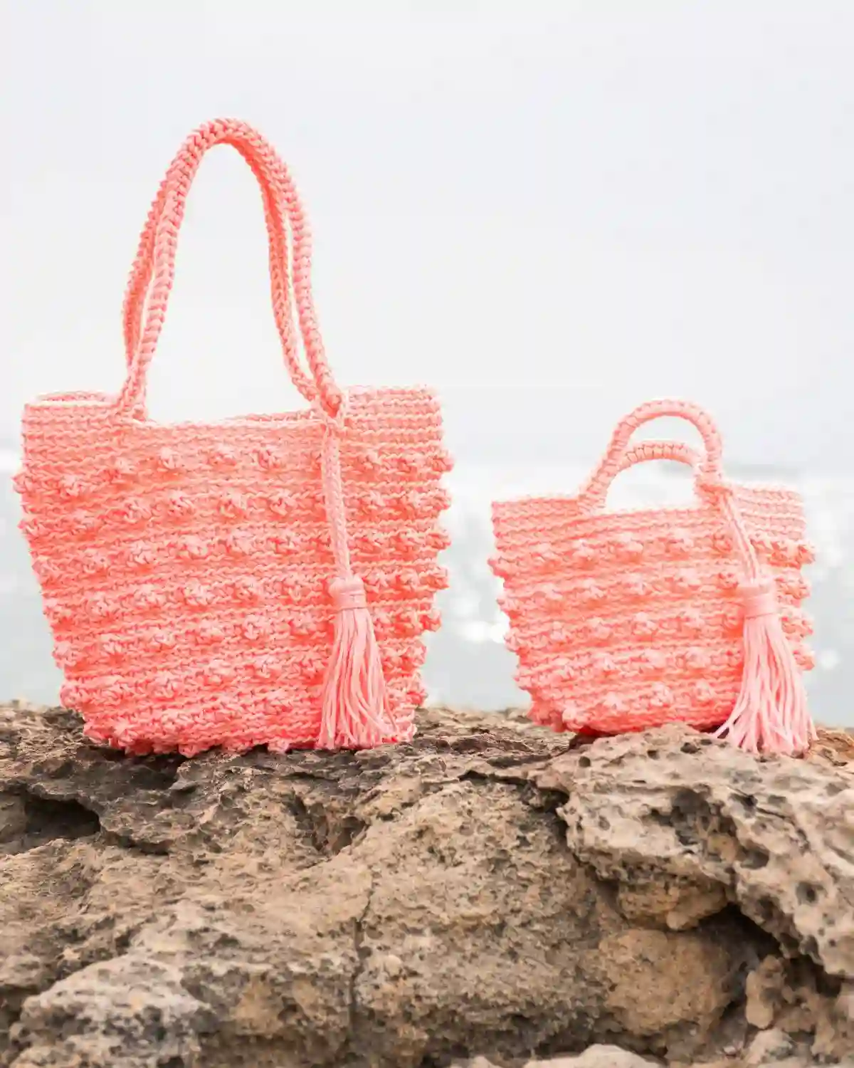 Dos formatos del bolso crochet de nudos rosa con asas tejidas y borla a juego.