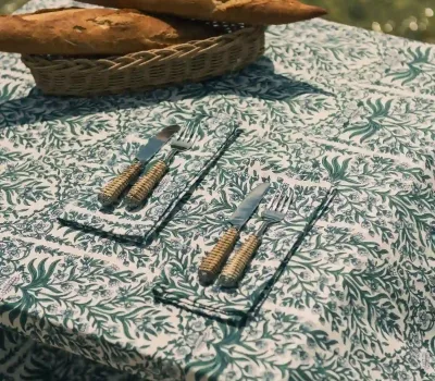 Mantel Enredadera Verde de algodón con estampado botánico en tonos verdes sobre mesa decorada junto al mar.