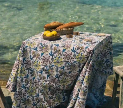 Mantel Cupido Gris de algodón con estampado floral en tonos gris, azul y verde sobre una mesa exterior junto al mar.