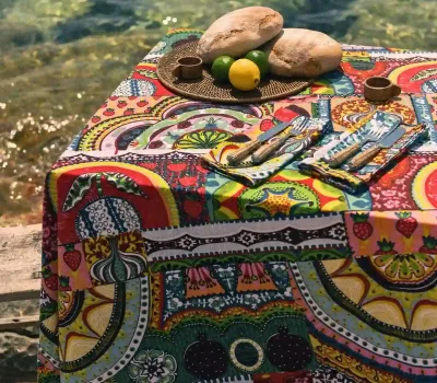 Mantel y servilletas Sicilia Multicolor de algodón de Cassai con estampado inspirado en la cerámica mediterránea sobre una mesa frente al mar.